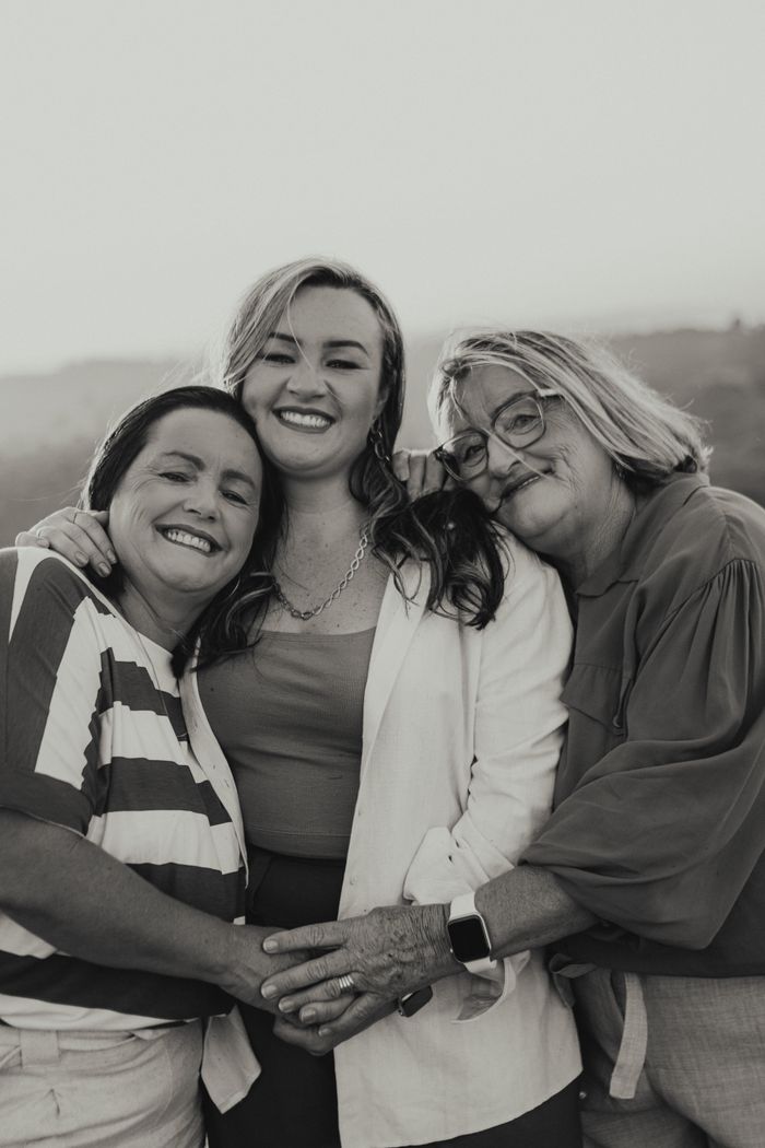 Three women of different generations smiling and embracing outdoors, symbolizing family love.